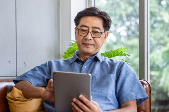 Senior Asian man using tablet connect internet while sitting on sofa at home - Powered by Adobe