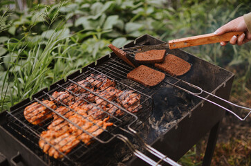 turning grilled pieces of bread and meat using an iron fork on a lake on a summer day