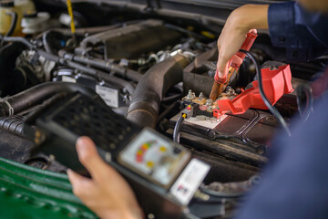 Auto mechanic checks car battery with battery checker in auto repair shop. Mechanics will work in the garage for customers who use their vehicles for repairs.