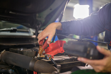 Auto mechanic checks car battery with battery checker in auto repair shop. Mechanics will work in the garage for customers who use their vehicles for repairs.