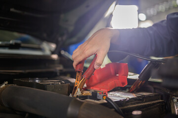 A car mechanic in an auto repair shop uses a battery checker to inspect the car's battery. When customers use the garage to get repairs for their vehicles, mechanics will work there.