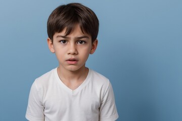 Young boy with angry or dissatisfied face standing against a blue background with copy space.