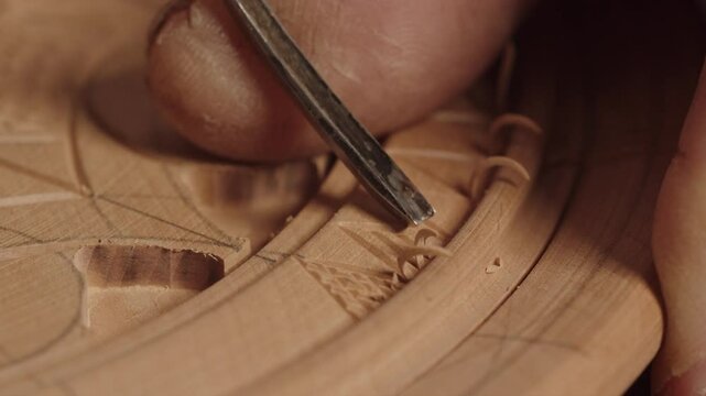 An artisan of wood carving uses a chisel to applying geometric rhombus shaped patterns on a wooden circle, holds the cutting tool with a finger. Handicraft concept as a hobby, skill, talent and
