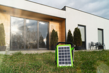 Small solar panel in green frame on lawn, contemporary home with large windows in background