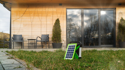 Green-edged solar panel on grass with stylish house and outdoor seating area behind