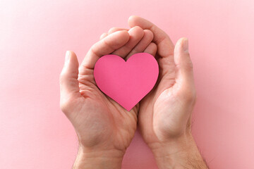 Two hands holding a heart-shaped cutout on a pink background