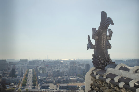 in front, a statue of a dragon-fish of a japanese castle, in the background, views of the city