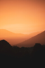 Stunning view of a dramatic sunset with beautiful shades of orange, silhouette of mountains in foreground and in the distance.