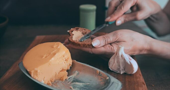A girl with a beautiful manicure is preparing sandwiches. Baguette, little butter, garlic on the table