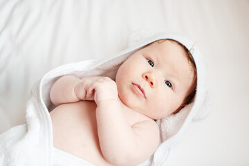 Portrait of a sweet little newborn baby girl after a bath in a white hooded towel. Baby care concept. 