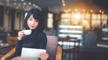 Beautiful attractive young Asian woman holding a cup of coffee or coffe in hand and sitting on sofa at cafe in the morning, vintage color tone.	
