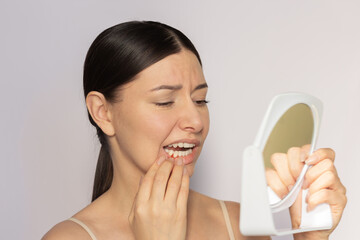 Young pretty caucasian woman looking at her red gums on her lower jaw in the mirror. She suffering...