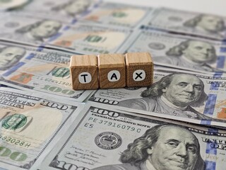 spelling the letters tax top of several US hundred dollar bills concept