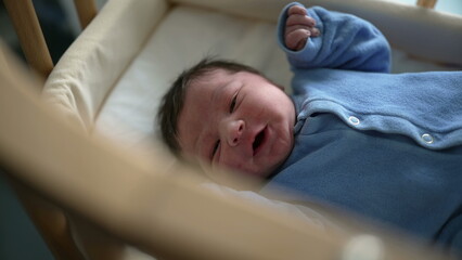 Adorable newborn in a blue onesie, lying in a crib, peacefully gazing around. Perfect for...