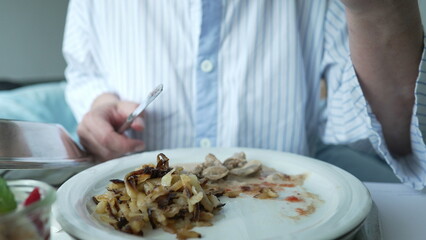 Close-up of a person in a hospital gown eating a meal on a tray, illustrating the daily routines and essential care provided to patients during their hospital stay for recovery