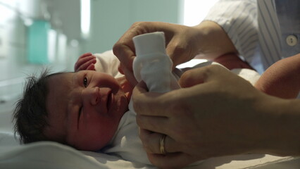 Newborn baby being gently dressed in a white onesie by caring hands in a hospital, showcasing the delicate and tender care given to newborns immediately after birth in a medical setting