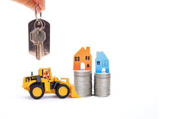 Miniature house on coin stack in front loader truck with hand holding key isolate on white background, new house, property investment, house loan