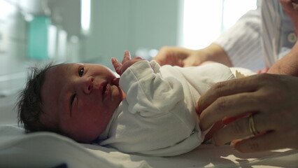 Obraz premium Newborn baby being gently dressed in a white onesie by caring hands in a hospital, showcasing the delicate and tender care given to newborns immediately after birth in a medical setting