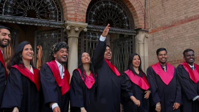 Graduating Indian students throwing graduation caps in the air. Friends wearing traditional academic gown, cap, celebrate academic achievement.