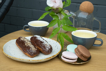 Eclairs and macarons with two cups of tea on table in cafe. Sweet food still life