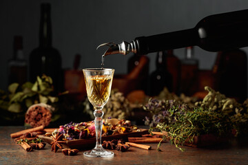 Yellow herbal liquor or mixture is poured from a vintage bottle into a glass.