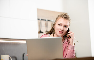 Young woman working from home using laptop and talking on phone