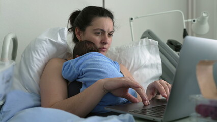 New mother multitasking in hospital bed with newborn baby, working on laptop, combining parenting...