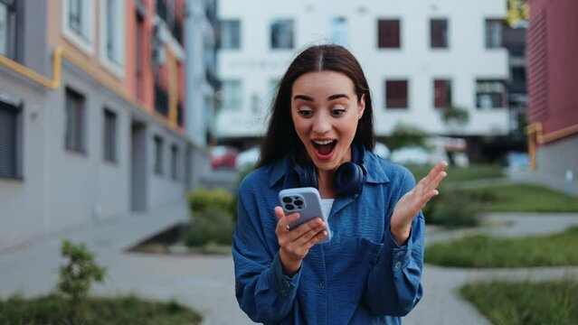 Excited young woman receives good news on her phone while walking outdoors.