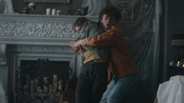 Full side shot of panicking friends rushing to tie up their girl friend with rope who being possessed by satanic being after performing invocation ceremony in abandoned house