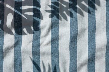 Tropical plants leaves shadows on the blue striped beach towel background