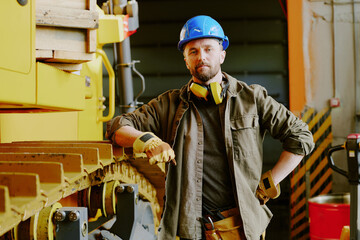 Medium portrait of confident Caucasian male technician in workwear standing by modern bulldozer looking at camera, copy space © AnnaStills