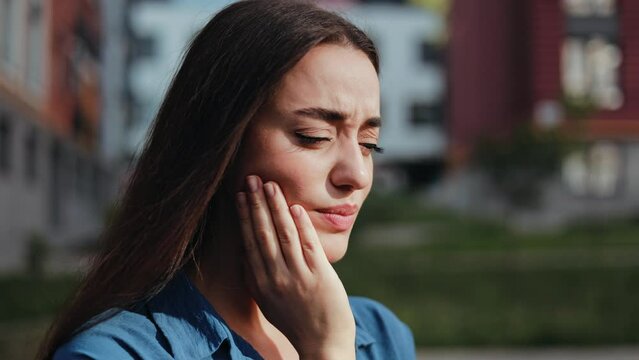 Young woman experiencing a painful toothache outside on a sunny day.