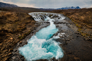 Fototapeta premium Bruarfoss Waterfall in Iceland with vibrant blue waters and a rugged landscape.