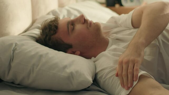 Caucasian man wake up looking mobile phone smartphone telephone gadget sleepy continue sleep lying on bed male weekend check time lazy daydream slumber nap resting technology device guy home bedroom