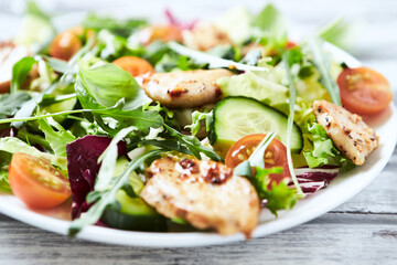 Salad with Chicken Breast, Cherry Tomatoes, Cucumber, Rocket and fresh Basil. Bright wooden background. Close up.
