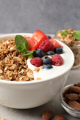 Tasty granola with berries and yogurt in bowl on grey table, closeup