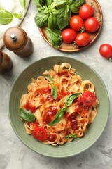 Delicious pasta with tomato sauce and basil in bowl on grey textured table, flat lay