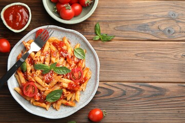 Delicious pasta with tomato sauce, basil and cheese served on wooden table, flat lay. Space for text