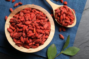 Dried goji berries and leaves on dark textured table, top view