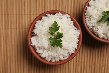 Bowls of delicious boiled rice with parsley on bamboo mat, top view