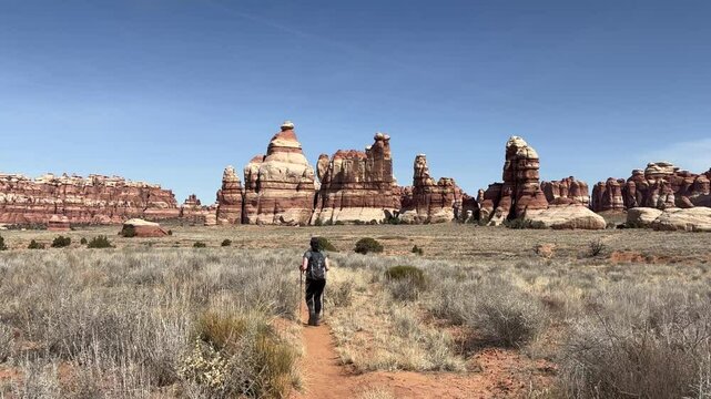 Slow motion tracking shot of a female hiker walking towards the needles sandstone formations in Canyonlands National Park, Utah. The beautiful desert landscape stretches out before her - USA