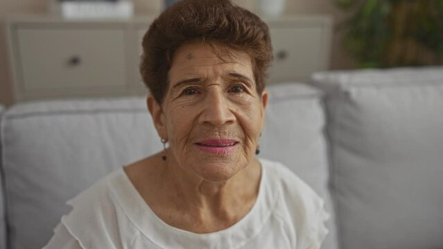 Elderly woman with short hair sitting in a comfortable living room, looking content and serene, capturing a moment of peacefulness at home.