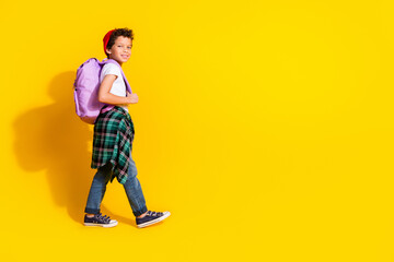 Full size photo of small charming boy backpack walk school wear trendy white outfit isolated on yellow color background