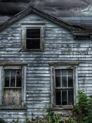 An old, weathered house with broken windows and peeling paint under a dark, ominous sky, suggesting abandonment and decay.