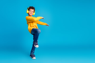 Fototapeta premium Full length photo of adorable little boy headphones dancing dressed stylish yellow garment isolated on blue color background