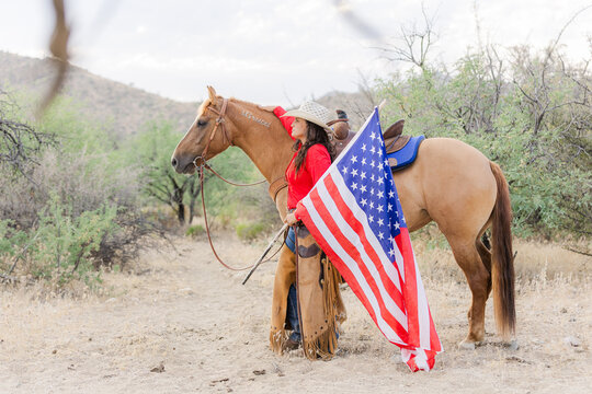 Cowgirl with her Mustang horse holding a US flag.