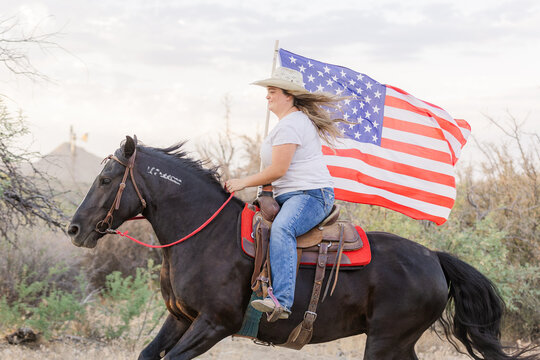 Cowgirl loping her Mustang horse carrying the US flag