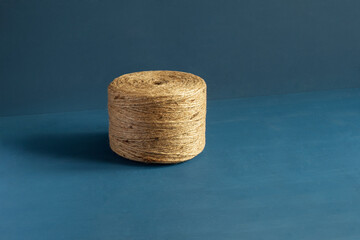 An insolated spool of natural fiber twine  natural color jute twine set against a striking hand-painted blue background with copy space focus on the twine’s texture.  Craftsmanship essence.