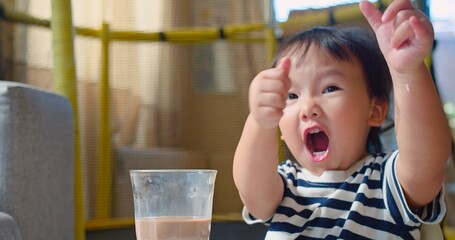 Adorable Toddler child Drinking Chocolate Milk in a Glass and Giving Thumbs Up Gesture Expressing showing Approval and Happiness at Home, Capturing a Sweet and Innocent Moment of Childhood