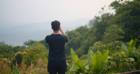 Fototapeta premium Man Taking a Photo with Smartphone in Nature, Capturing Scenic Landscape Outdoor Photography, Greenery Trees and Mountains in the Background, Peaceful and Serene Environment